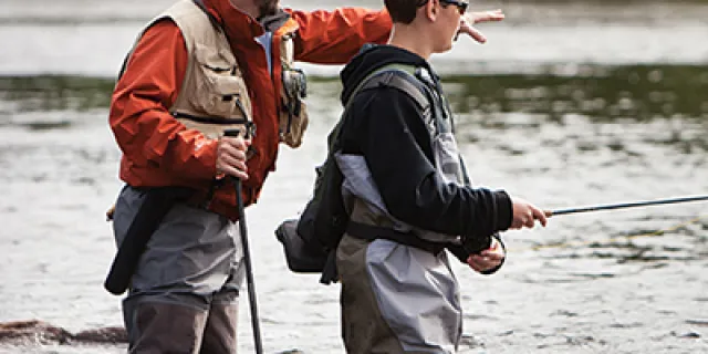 Father teaching son how to fish in river bank. 